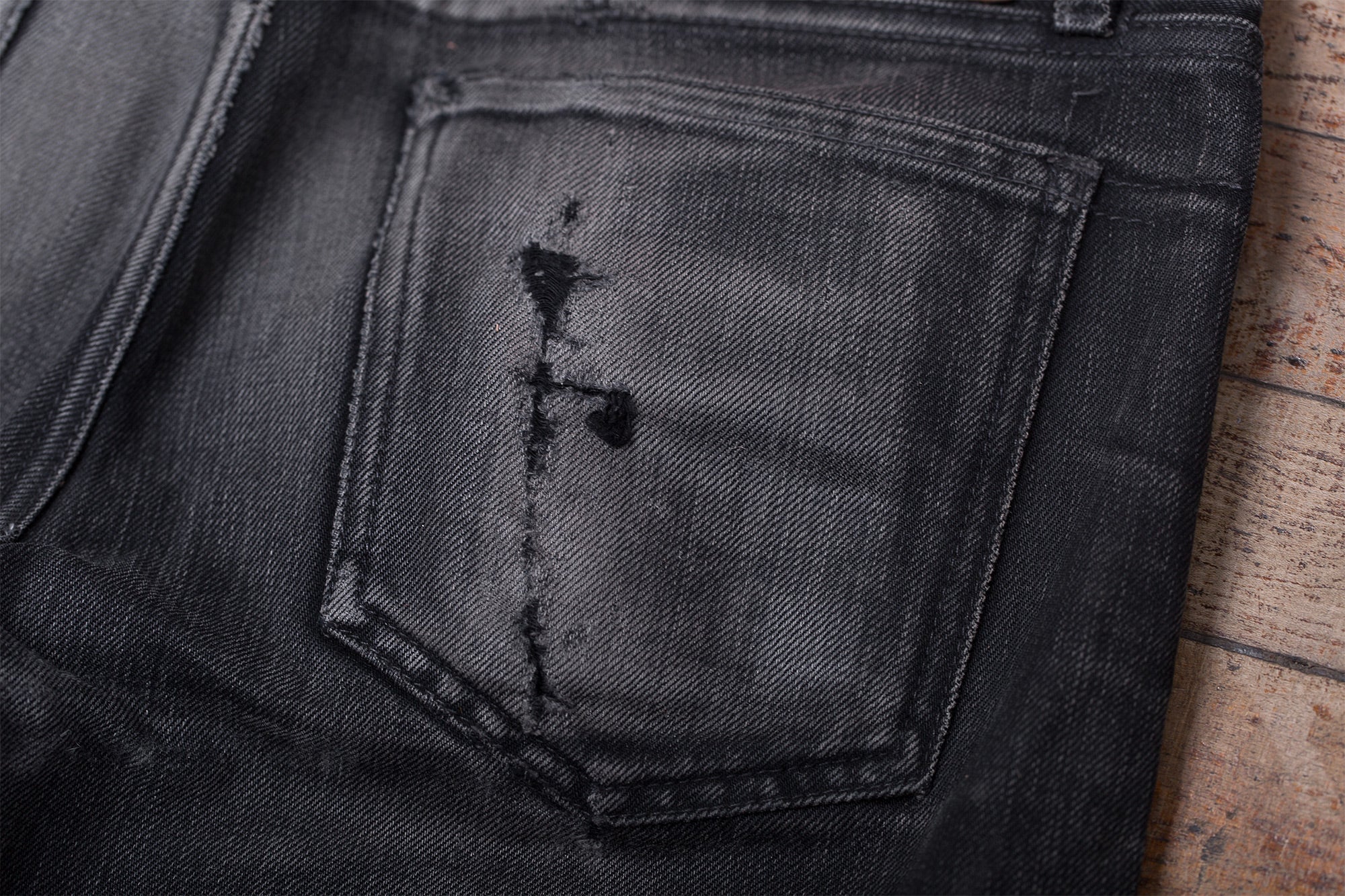 Detail photo of a pair of worn-in black jeans laying on a wooden floor.