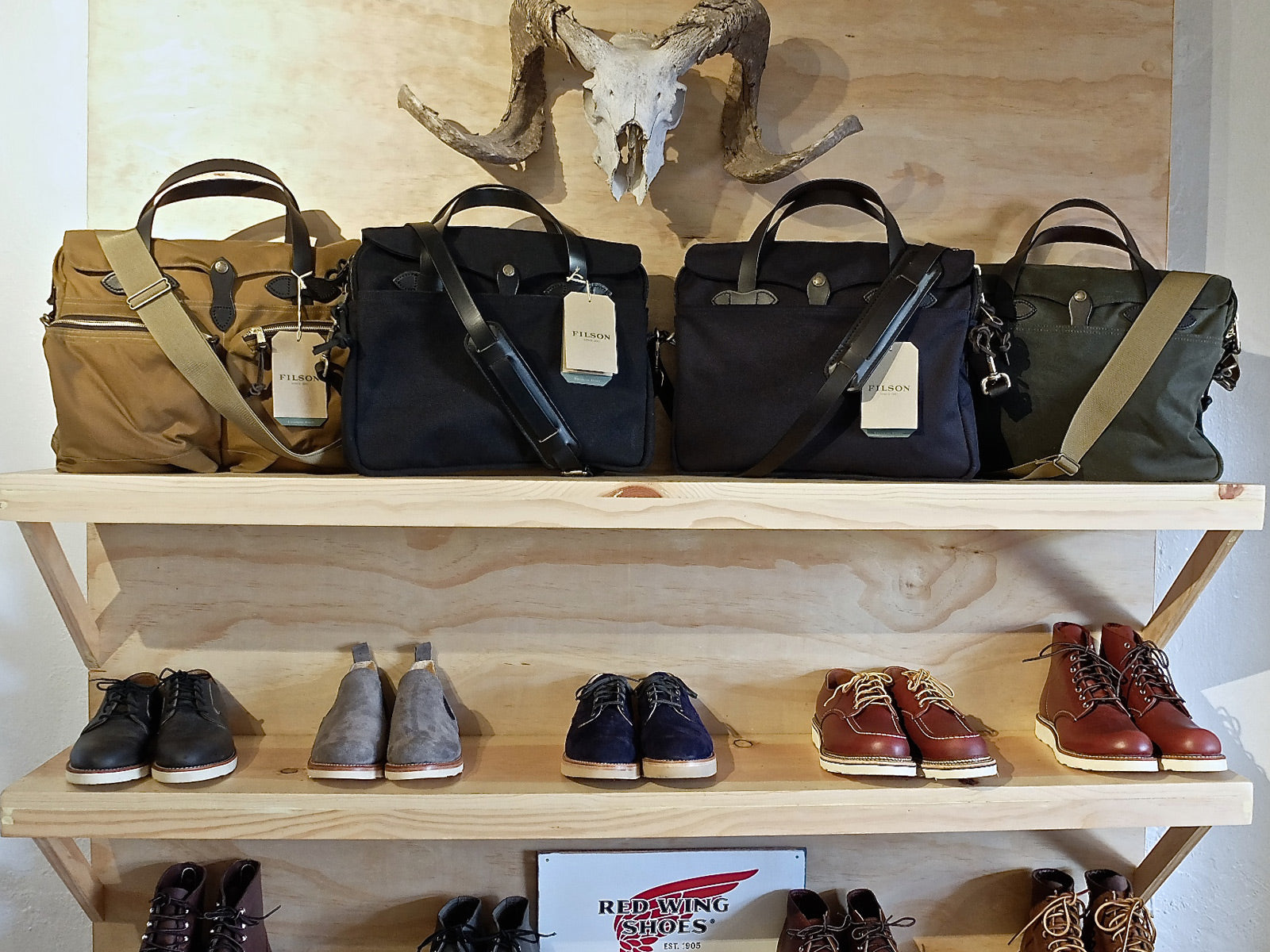 Wooden racks displaying Red Wing shoes and Filson bags beneath a cow's skull.