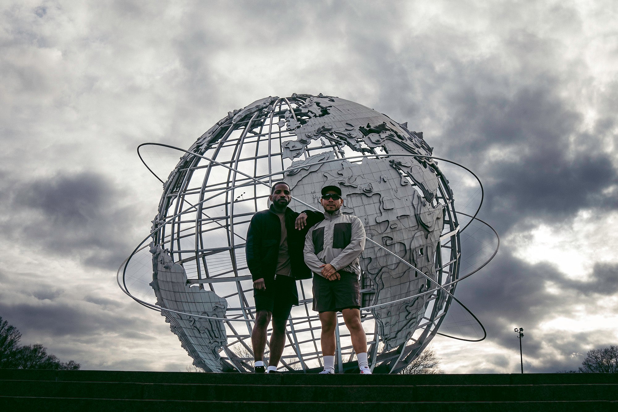 Two men pose by the unisphere in Flushing Meadows park.