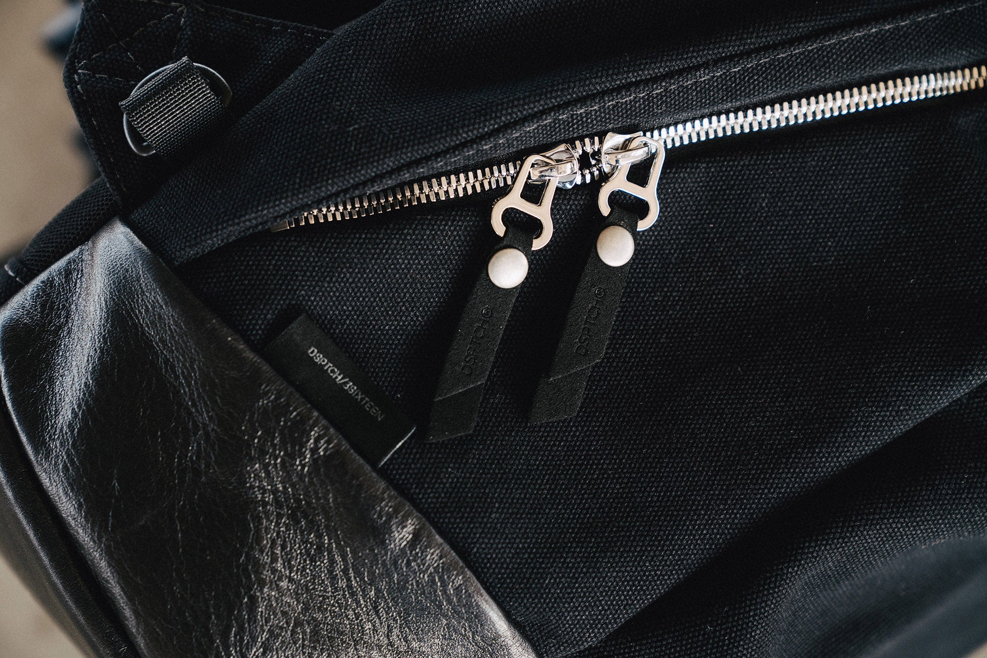 A close up photo of a black canvas backpack with shiny silver zippers.