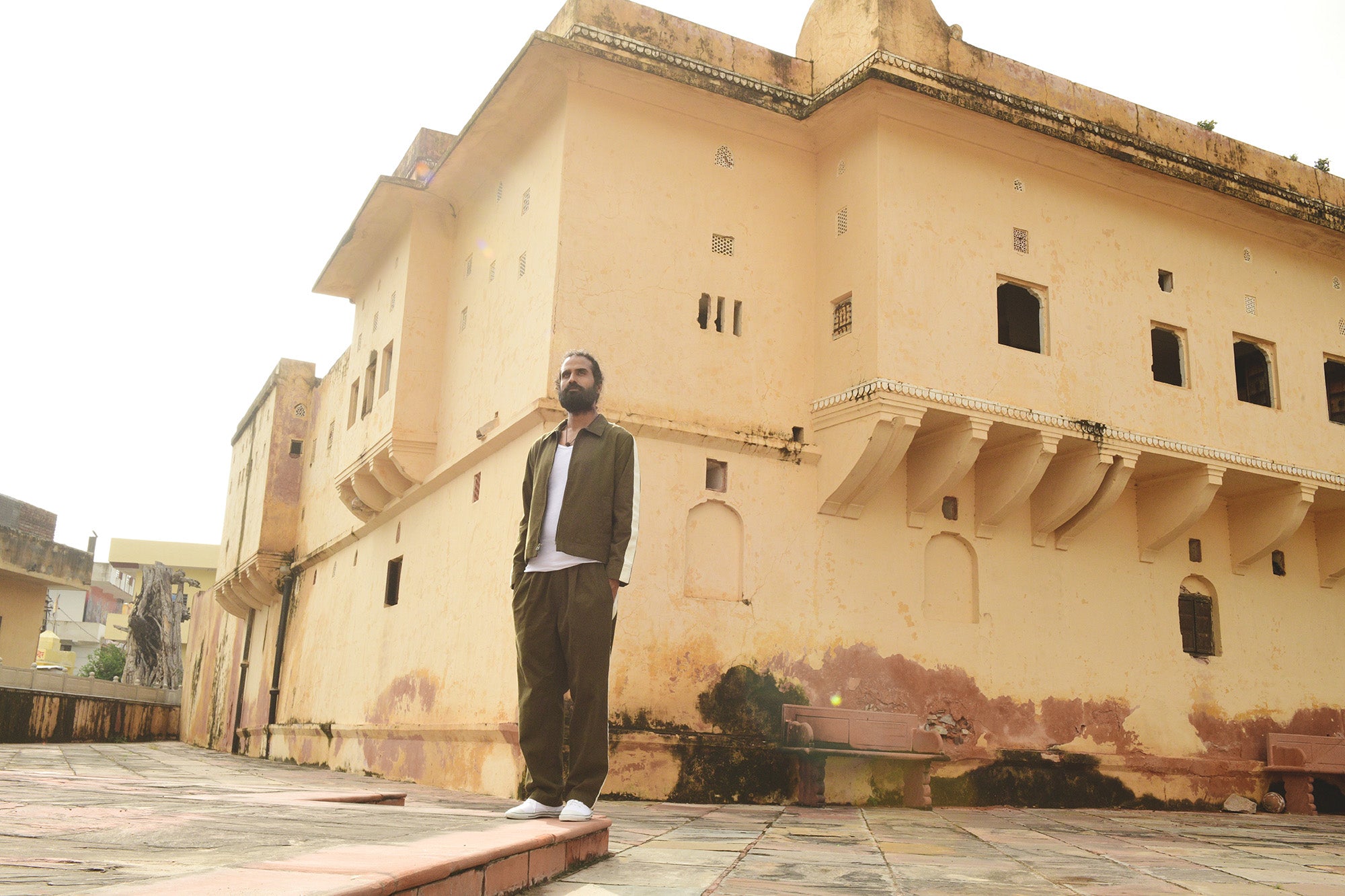 A man stands on a corner of a building with the sun shining from behind him.