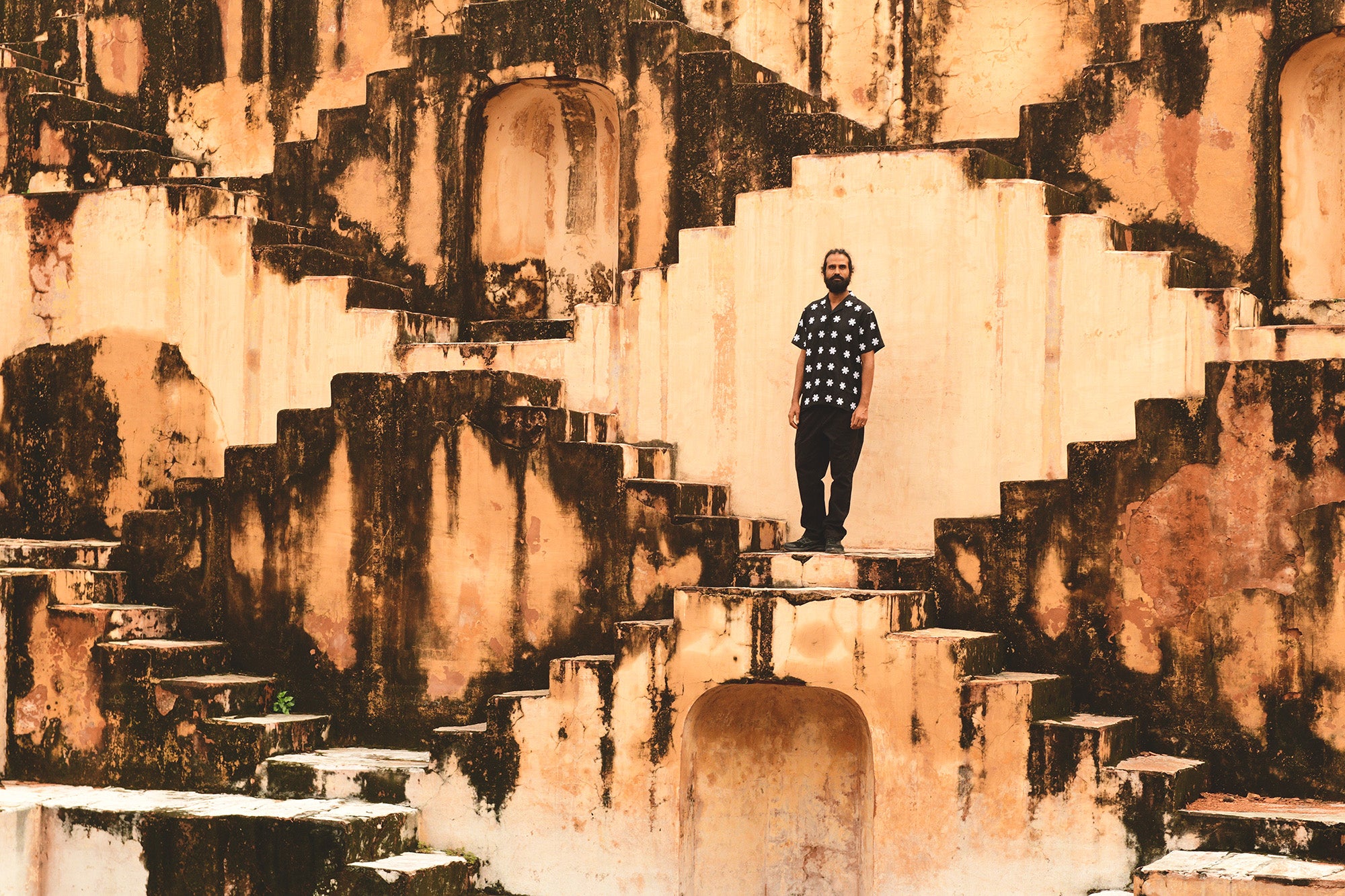 A man in a black shirt and pants poses on some huge stone steps.