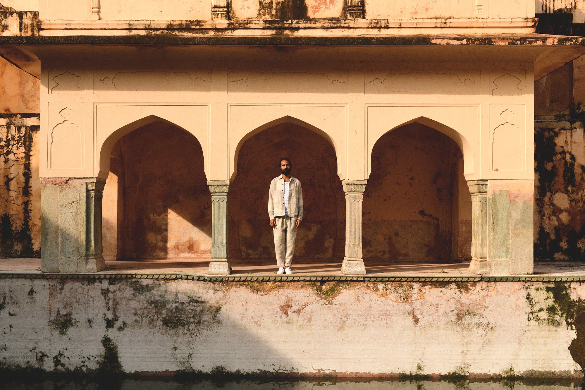 A man in a grey jacket and pants stands in a centuries old archway.