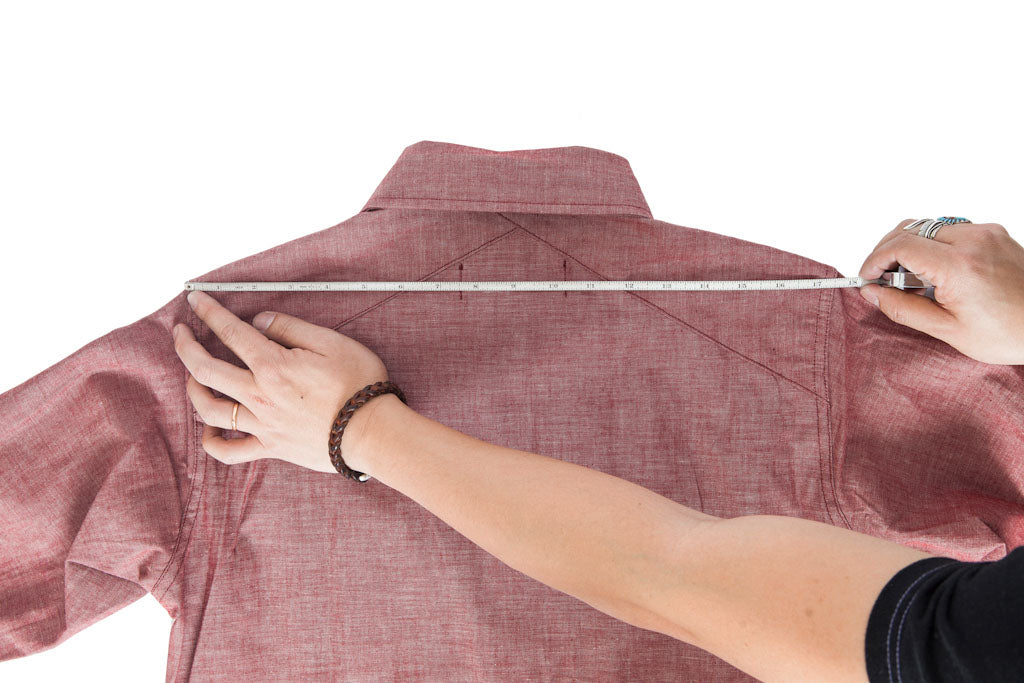 A tape measure running across the back of a shirt from shoulder seam to shoulder seam at the top