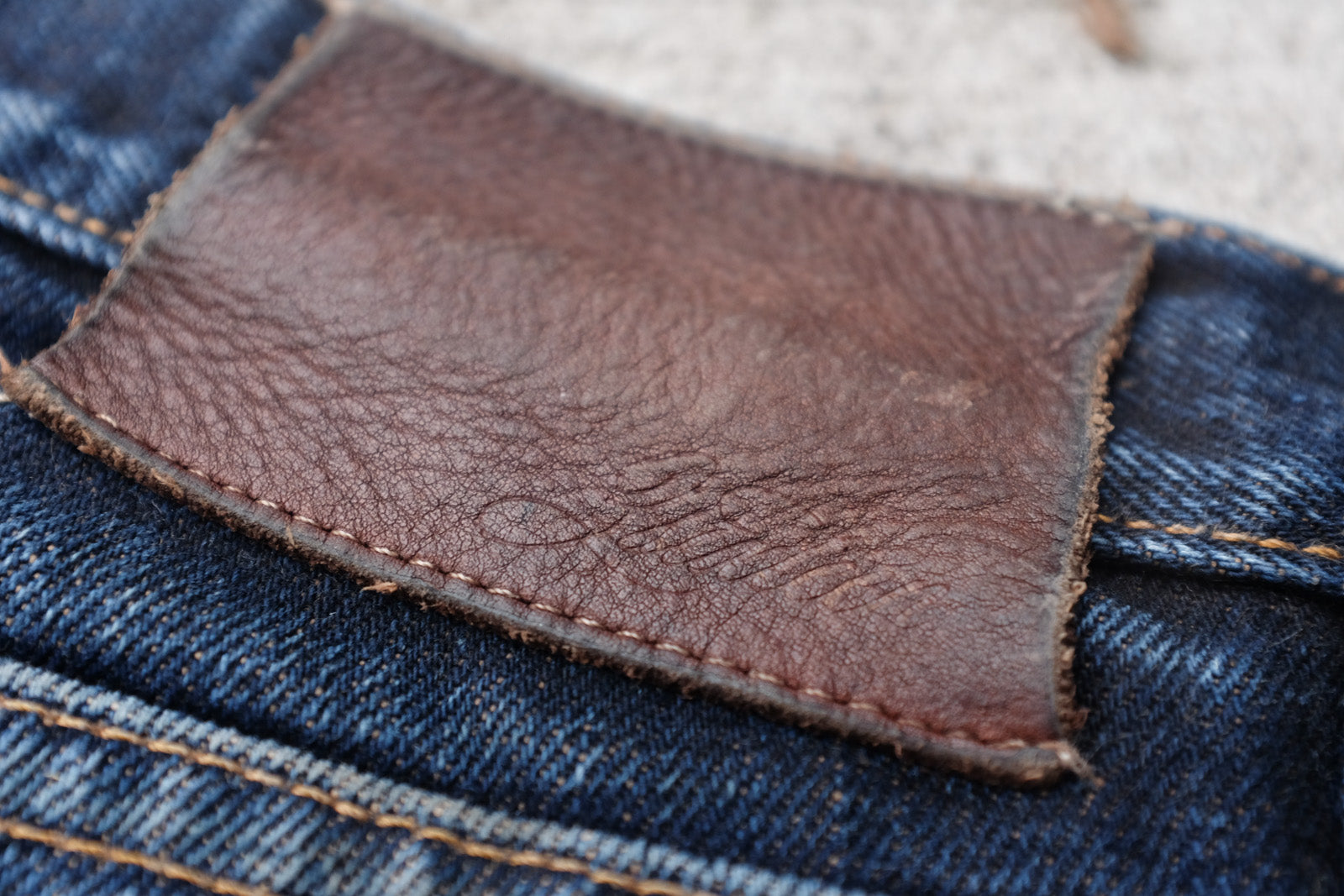 Detail photo of the worn leather patch on the rear of the jeans which has darkened and developed a scale-like pattern as it has aged.