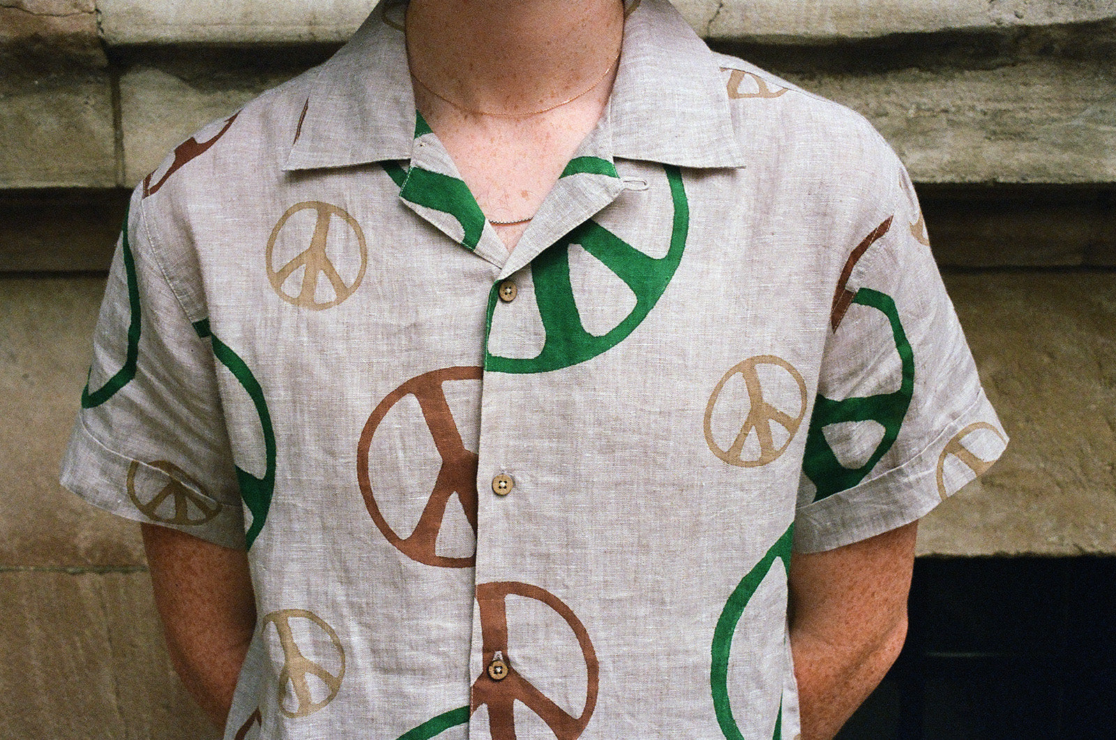 A close up image of a tan shirt with various colored peace signs printed on it. 