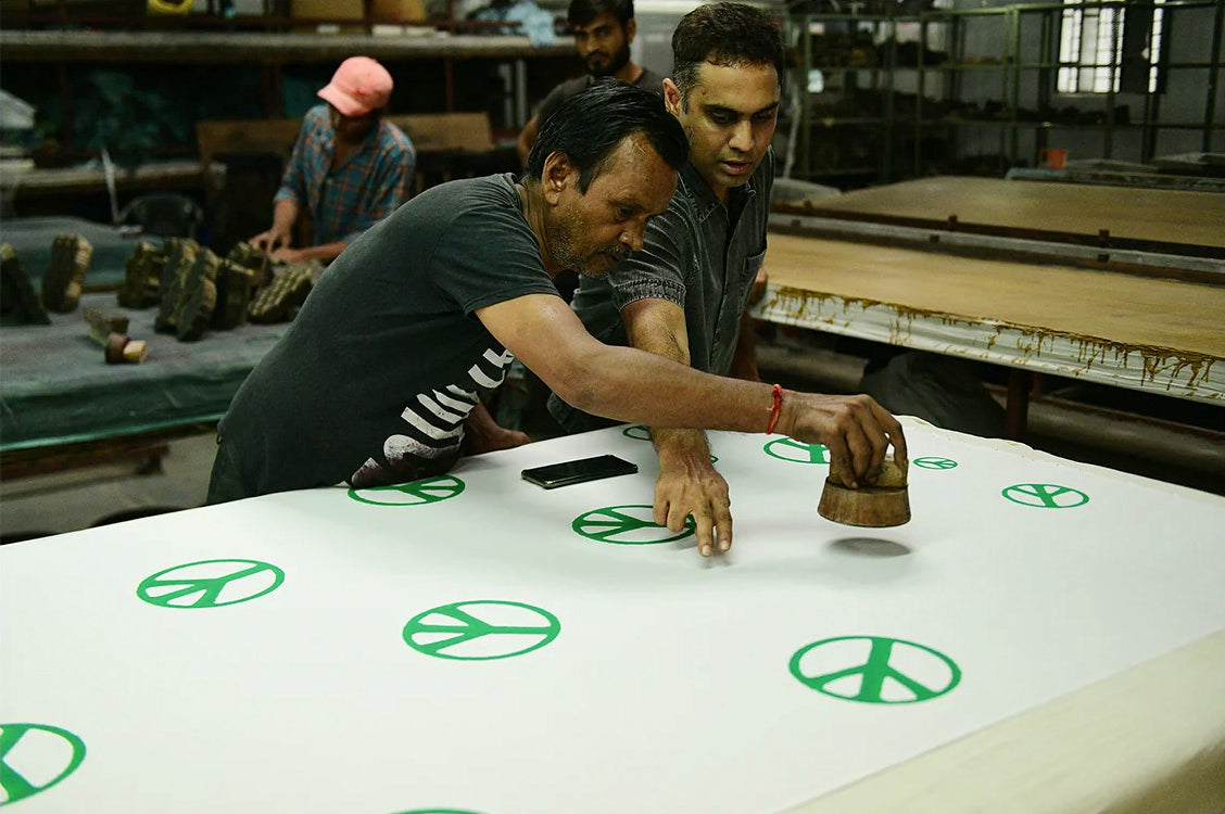 Two men inspect a block print and discuss strategy.