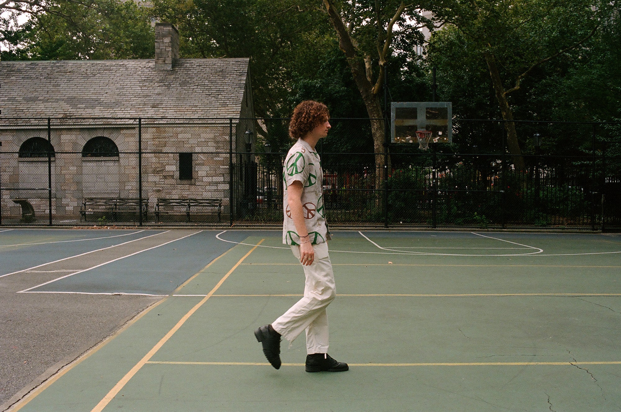 A man in a colorful peace shirt walks across a basketball court.