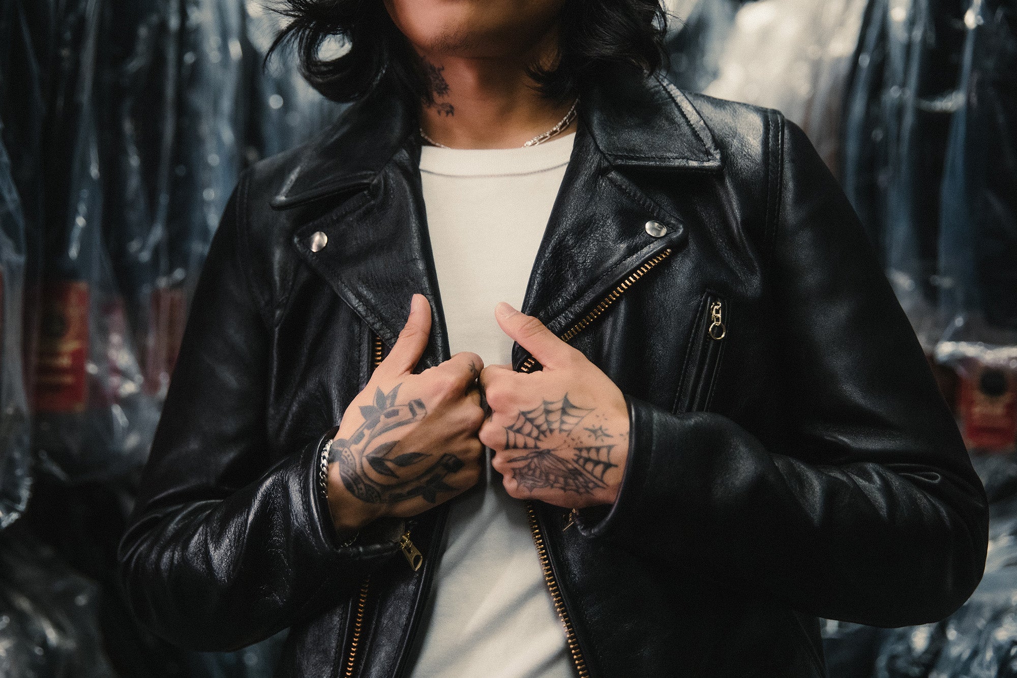 A close shot of a shiny black leather jacket with hands with tattoos on them