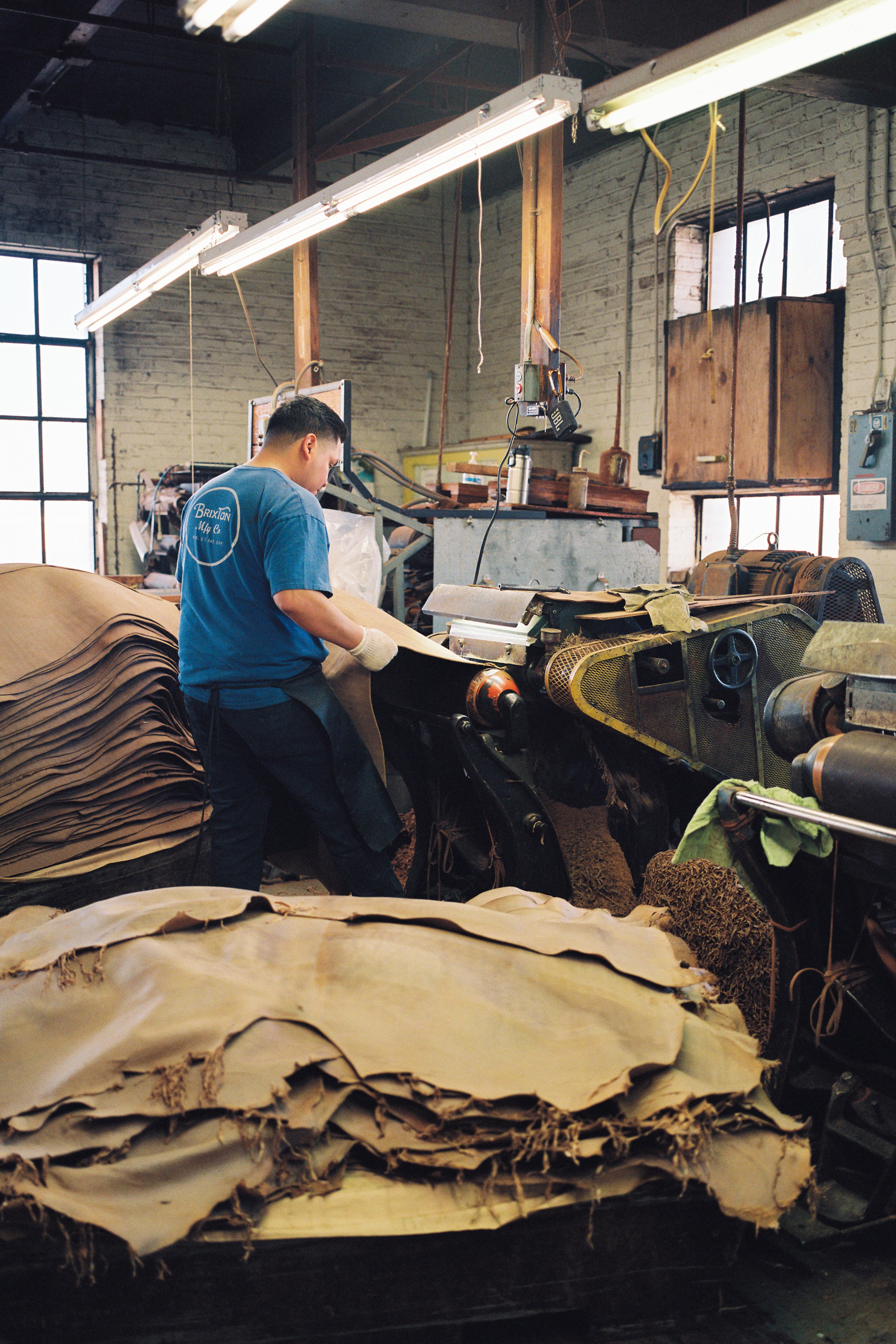 A man trims down leather at a machine.