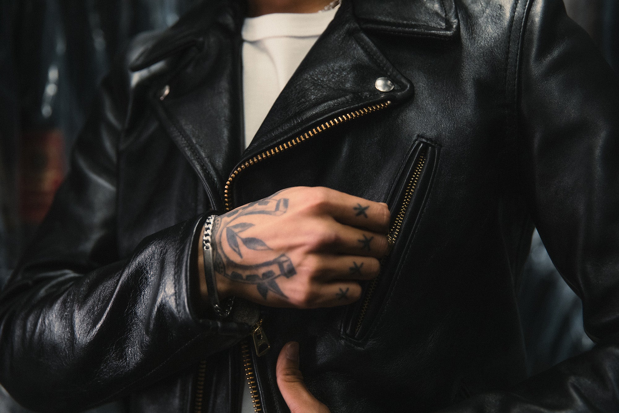 A tight shot of a man unzippinga leather jacket.