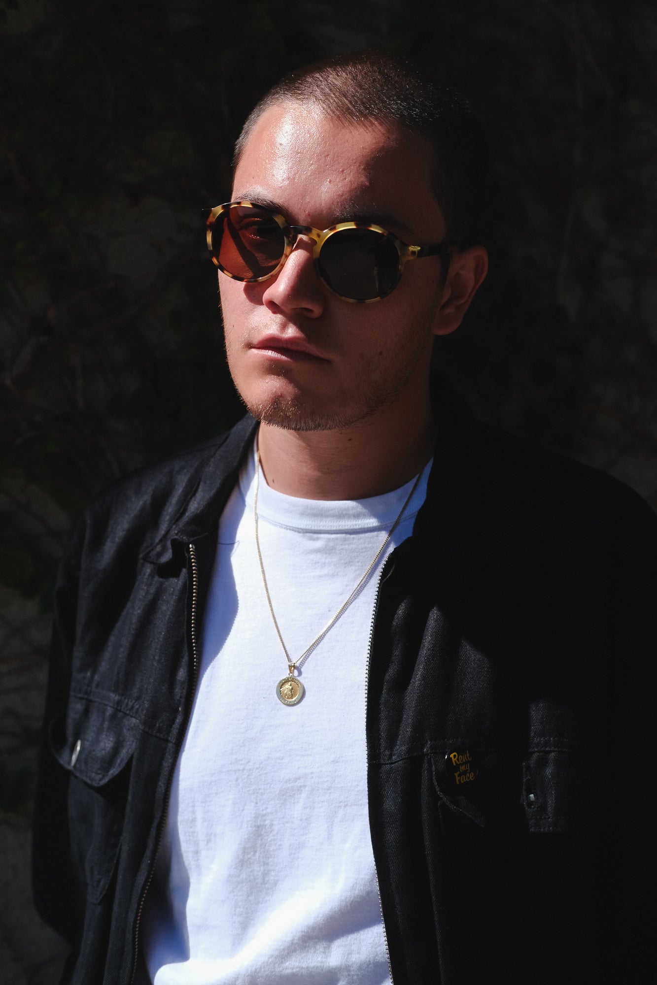 A man in sunglasses and a white tee stands in dramatic light.