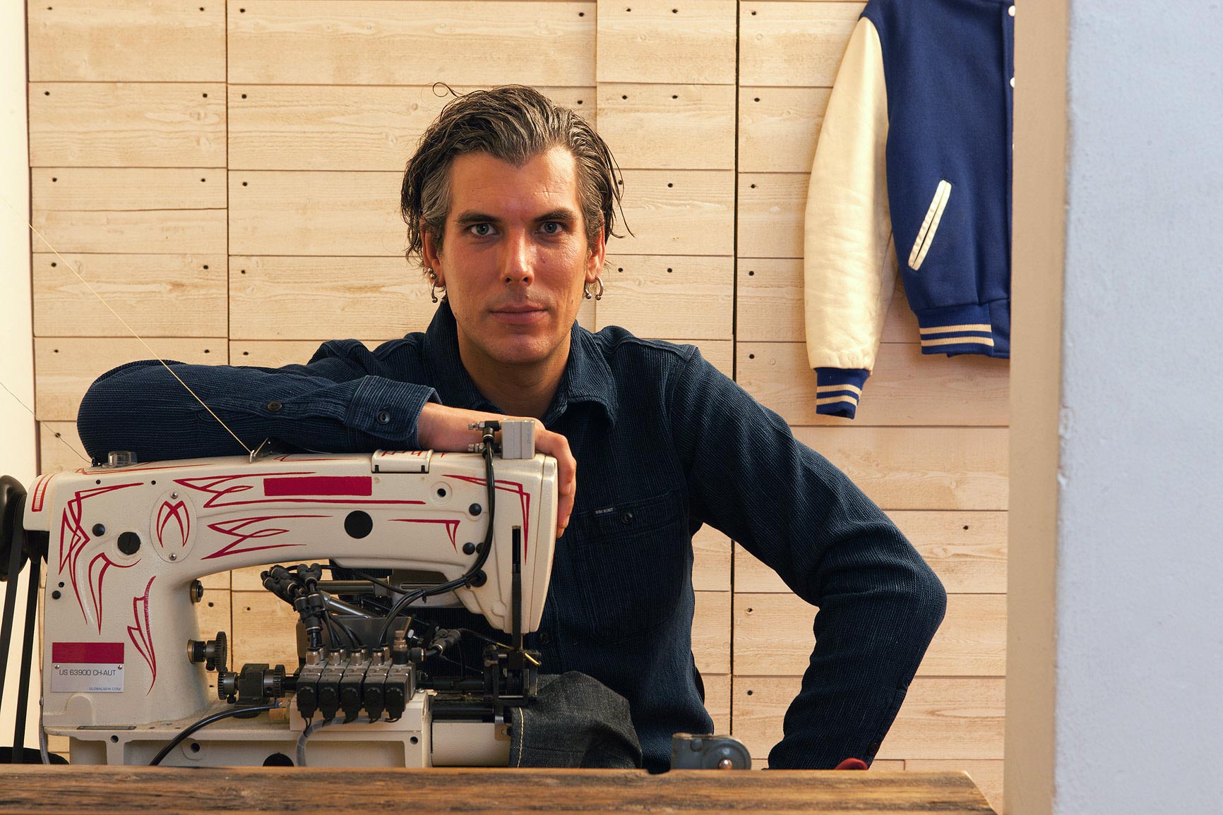 Man posing over chainstitch sewing machine.