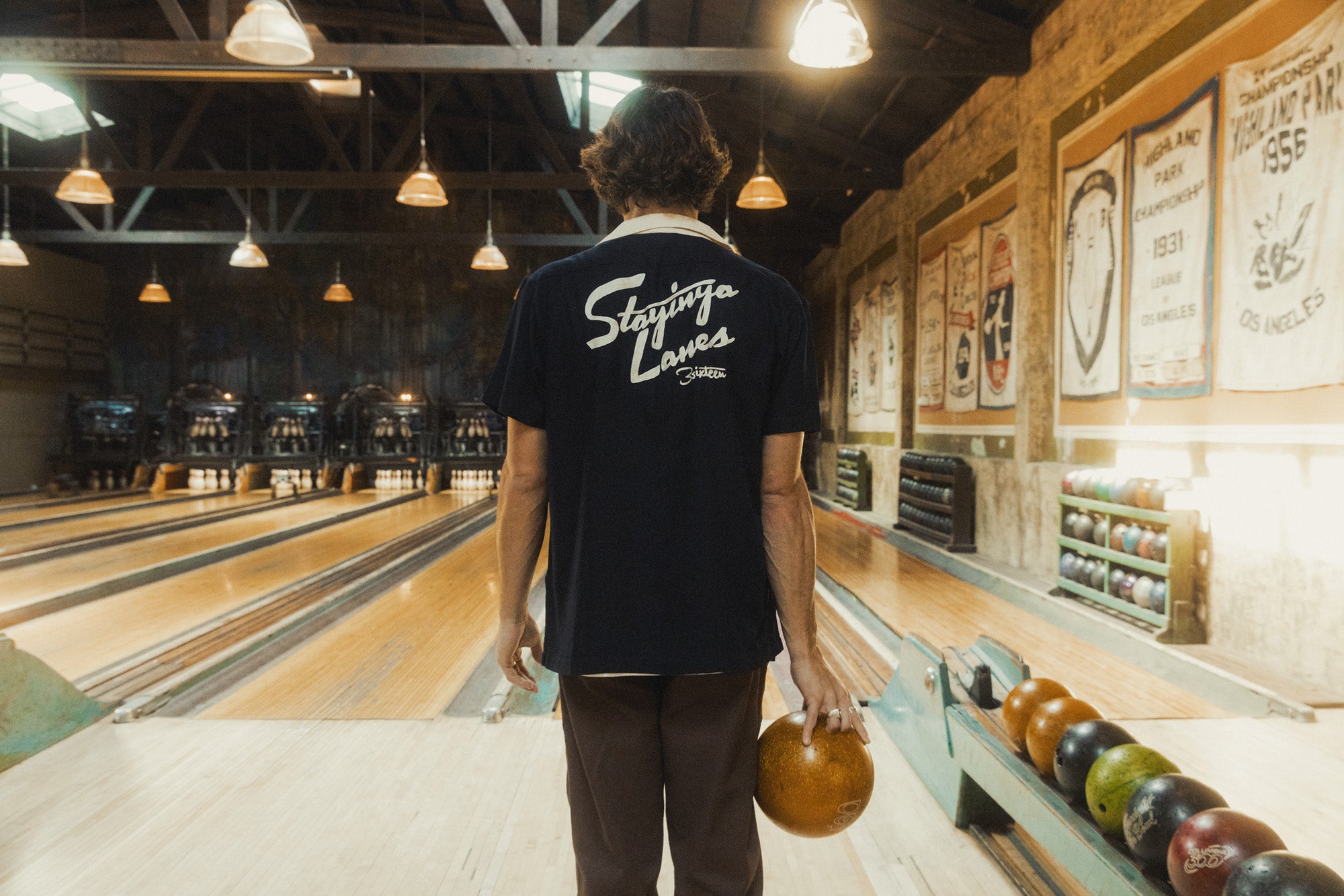 A man stands with a bowling ball in hand in an old bowling alley.