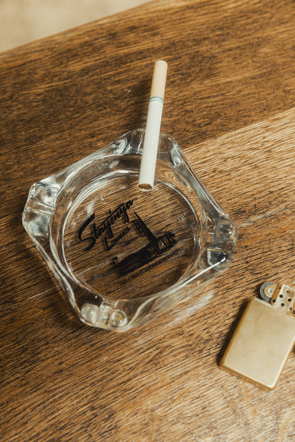 A glass ashtray with a bowling alley printed on it sits on a wooden table.
