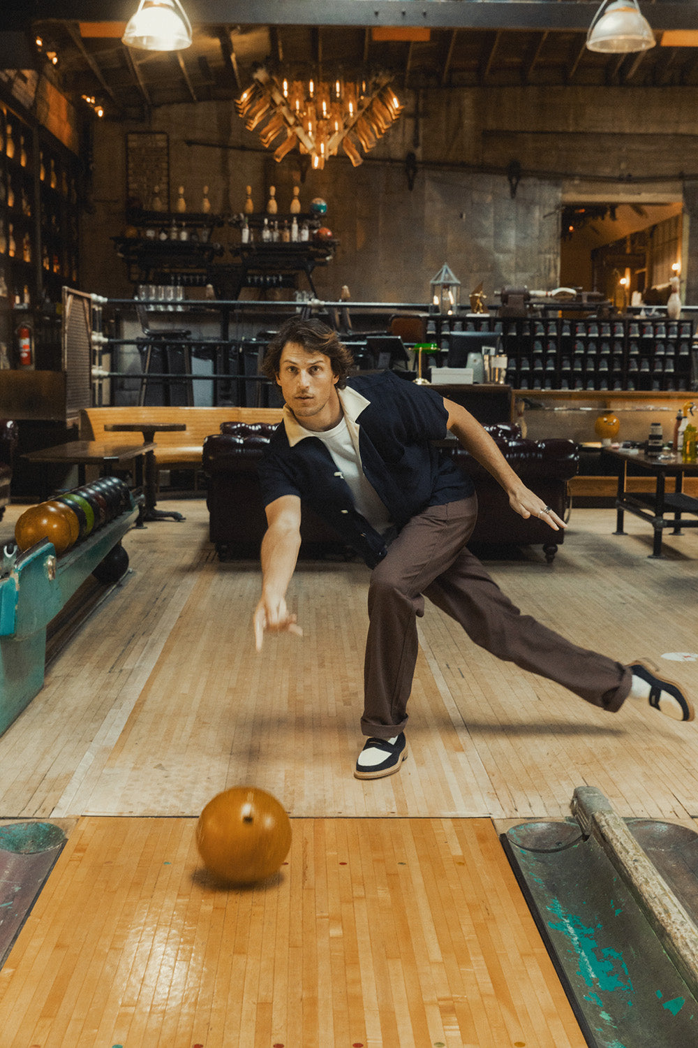 A man in a navy shirt bowls a ball down a lane.