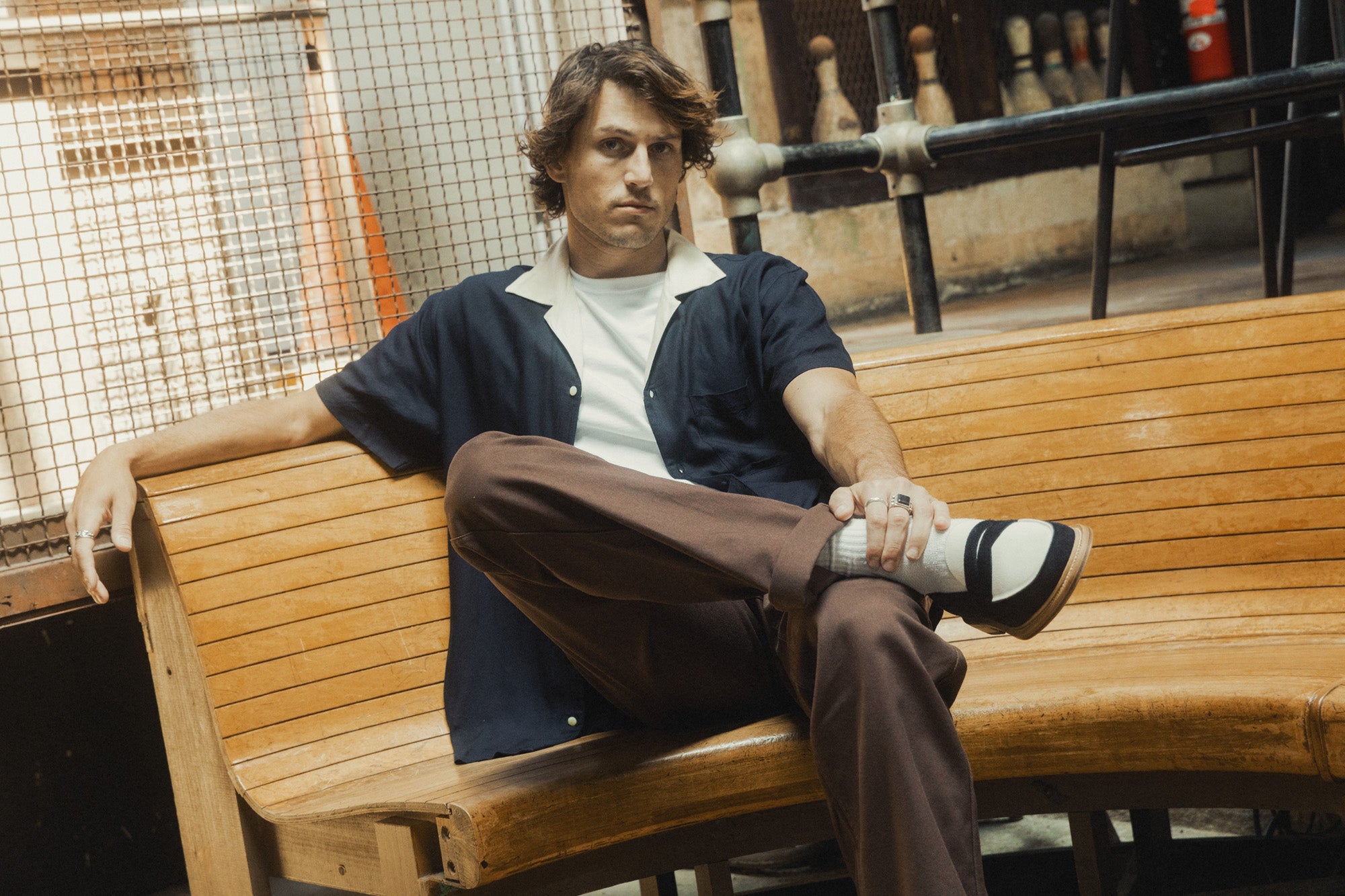 A man in a navy shirt and brown pants sits on a wooden bench.