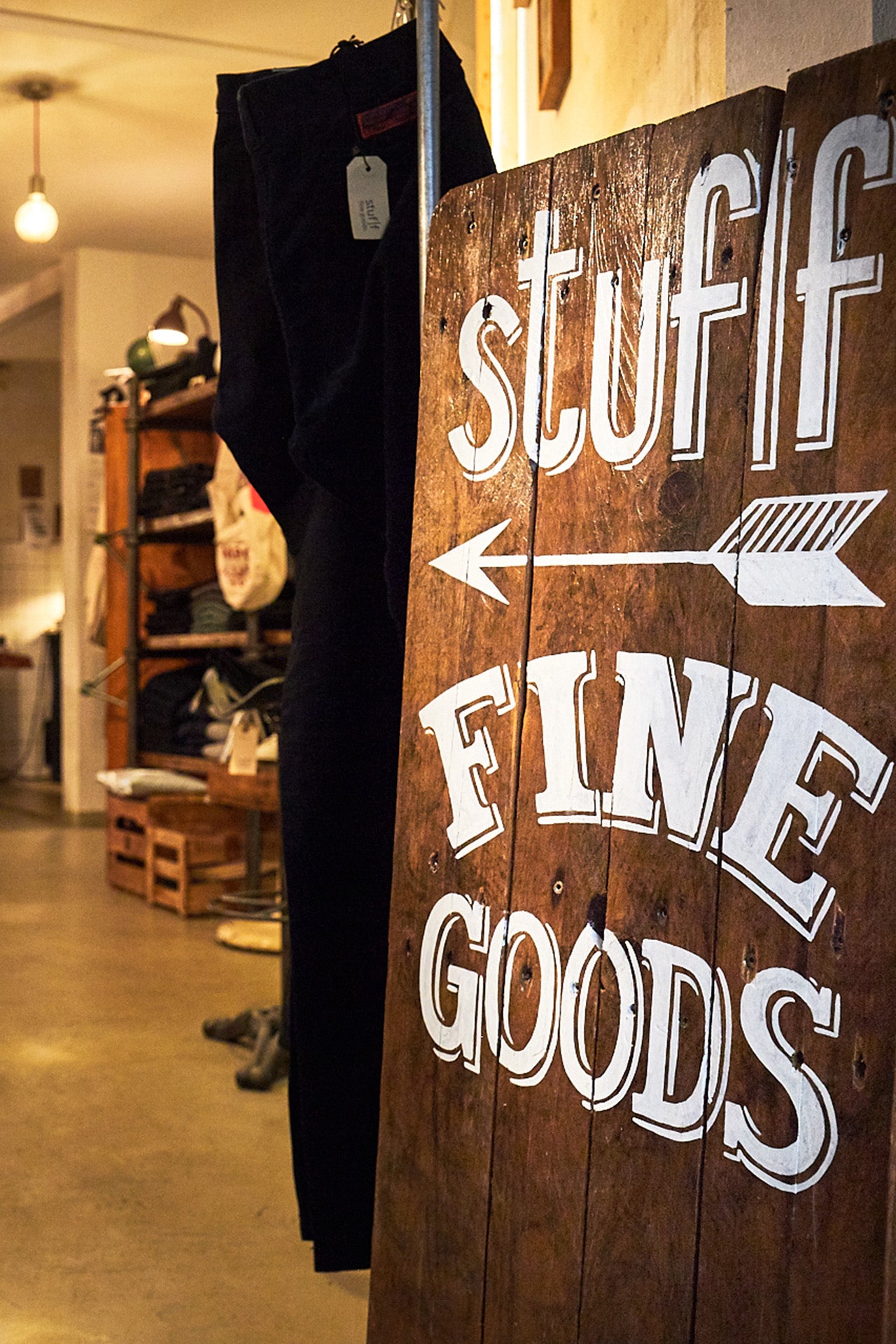 A hand painted wooden board that says 'Stuff Fine Goods' on it.