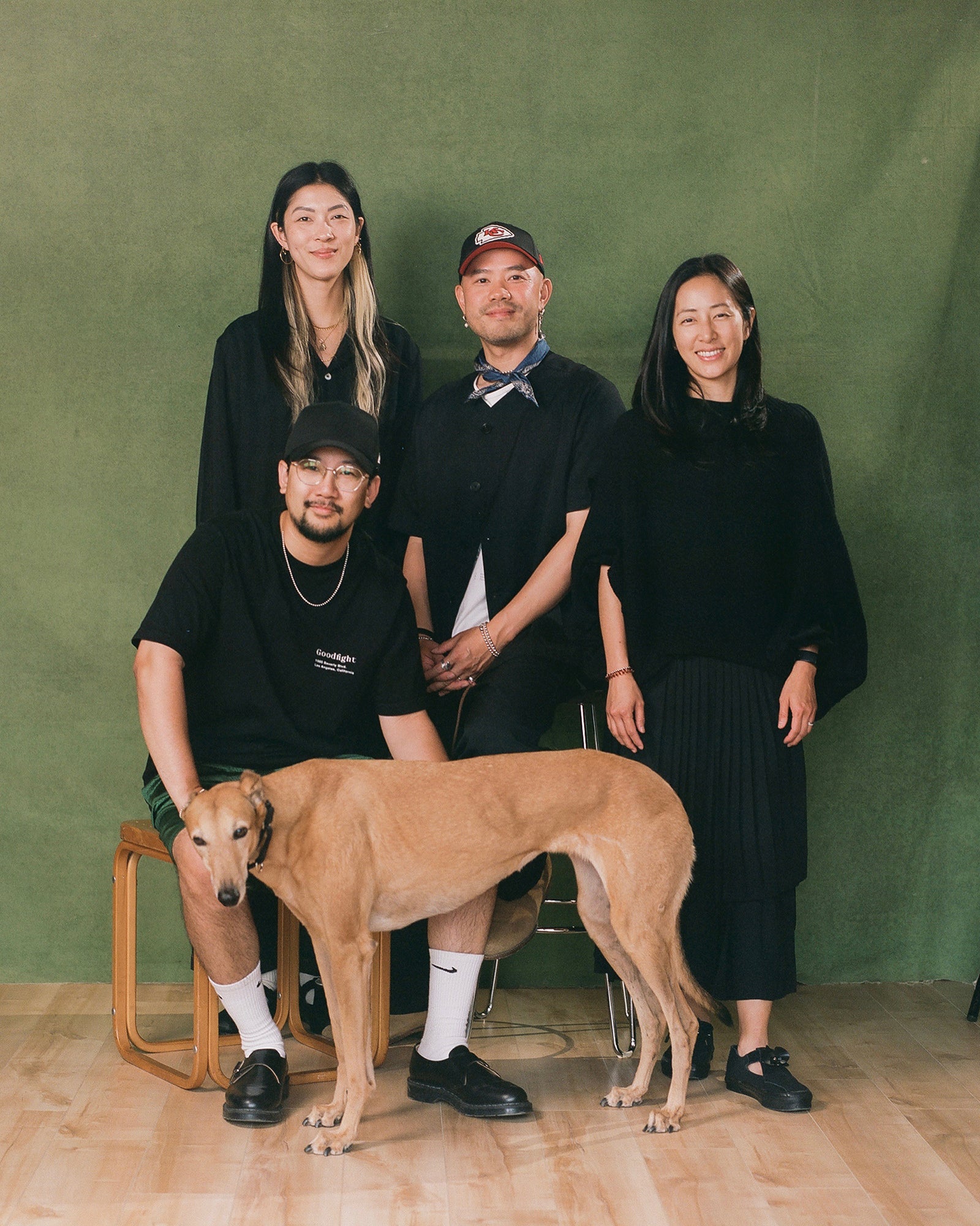 Four stylish asians and a dog pose in front of a green backdrop.