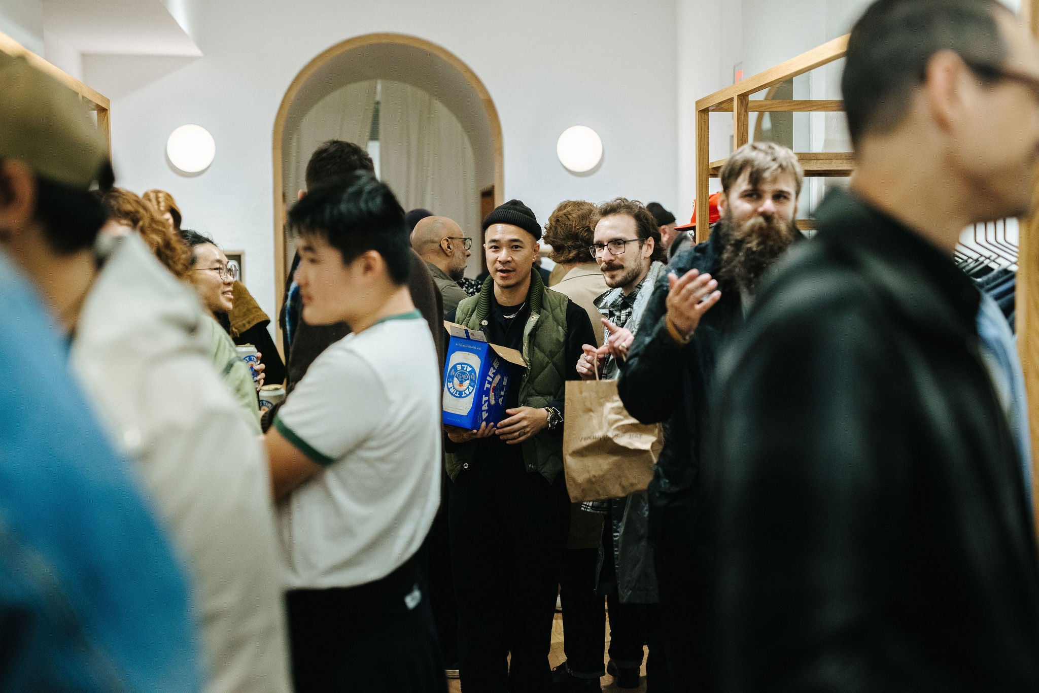 an image of a man carrying a case of beer through a crowded room.