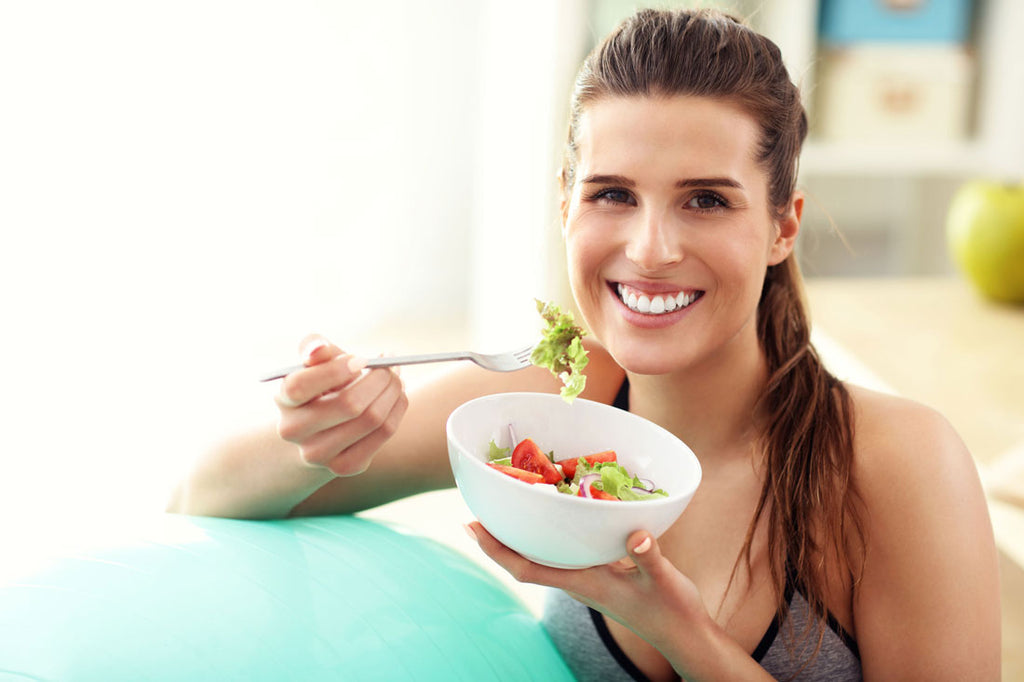 Image of a woman smiling and eating a salad