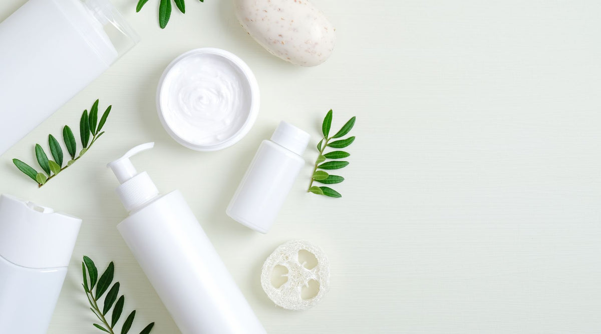 white skincare bottles and jars surrounded by decorative ferns