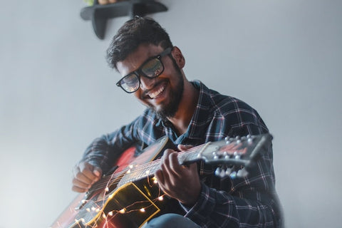 Man wearing blue flannel playing guitar.