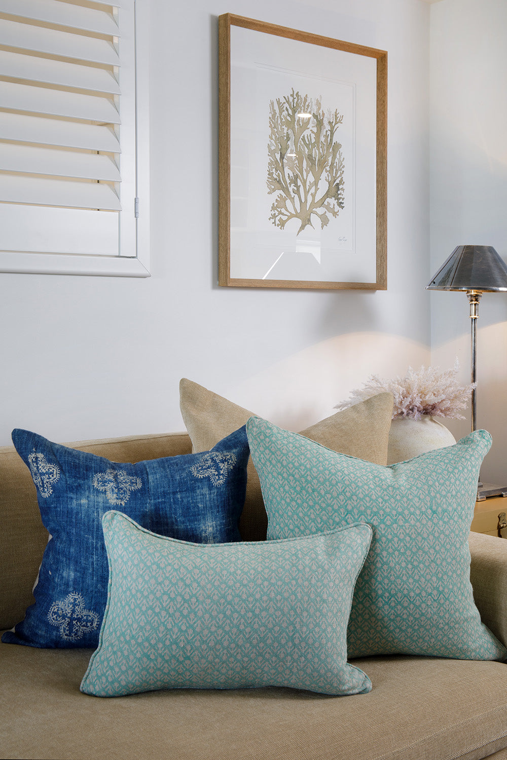 Styling by Rachel Elizabeth Interiors & Textiles. Living room feature beige couch, rattan coffee table, numerous cushions, rug, lamp and wall art