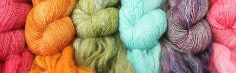 a close up overhead shot of a mini rainbow of yarns - a skein each of red, orange, green, blue, purple and pink.