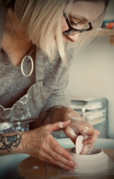 Image shows Kirsty at work on her potter's wheel, deep in the process on creating a beautiful porcelain pot.