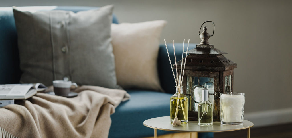 Candle, Diffuser and Room Spray on small table in living room with navy couch, neutral blanket and cushions in background.