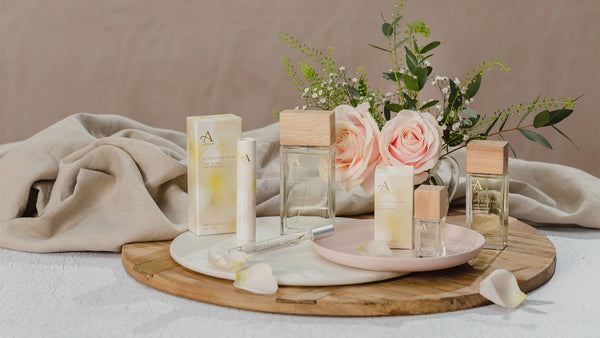 Full range of After the Rain Fragrances in glass bottles, displayed on top of a table with pink roses