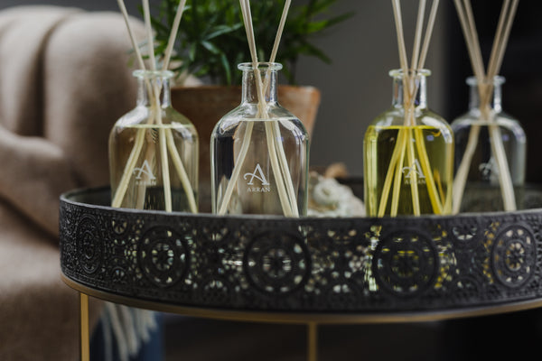 Image shows 4 reed diffusers, the oil colour varies from clear to yellow. They sit on top of a sidetable.