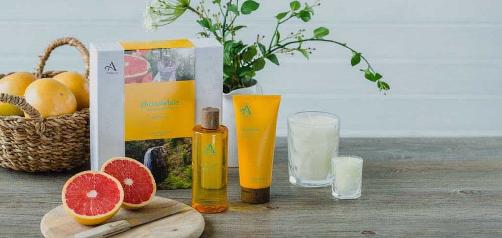 Image of citrus shower gel, body lotion and candles on wooden table with sliced grapefruits in background