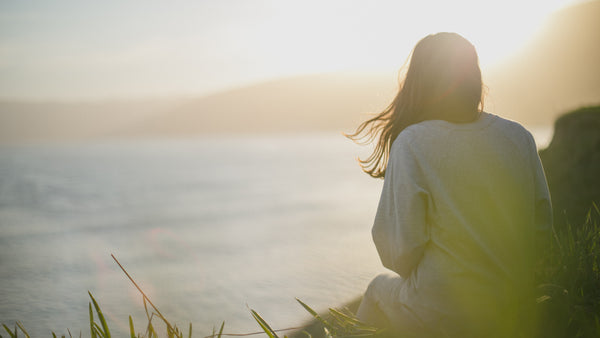 Woman looking out from cliffside across the sea at sunset