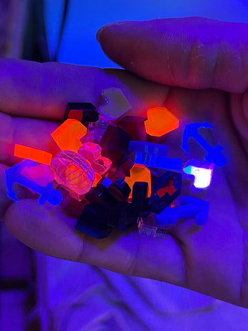 A handful of colorful earrings, which are glowing under a blacklight.