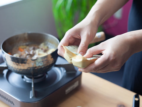 Hände zerschlagen eine Packung Curry-Mehlschwitze-Blöcke.