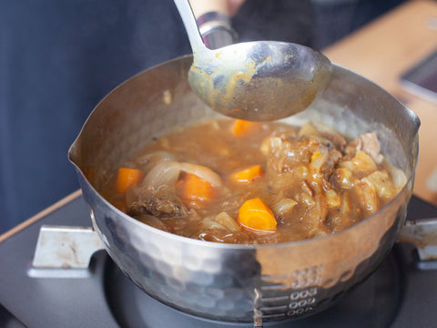 Schöpfkelle wird über einen Topf mit japanischem Curry gehoben.