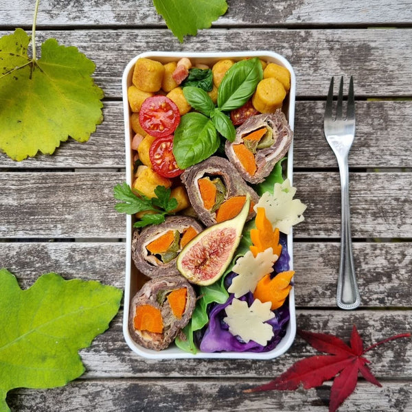 Almuerzo bento con temática otoñal que incluye ñoquis de calabaza con panceta, espinacas y tomates cherry, rollitos de carne, col lombarda salteada y recortes en forma de hojas de zanahorias y queso.