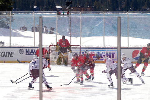 A hockey game being played outdoors in the snow with a large crowd in the stands