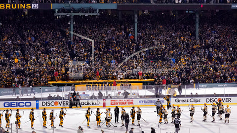 A hockey game being played outdoors in the snow with a large crowd in the stands