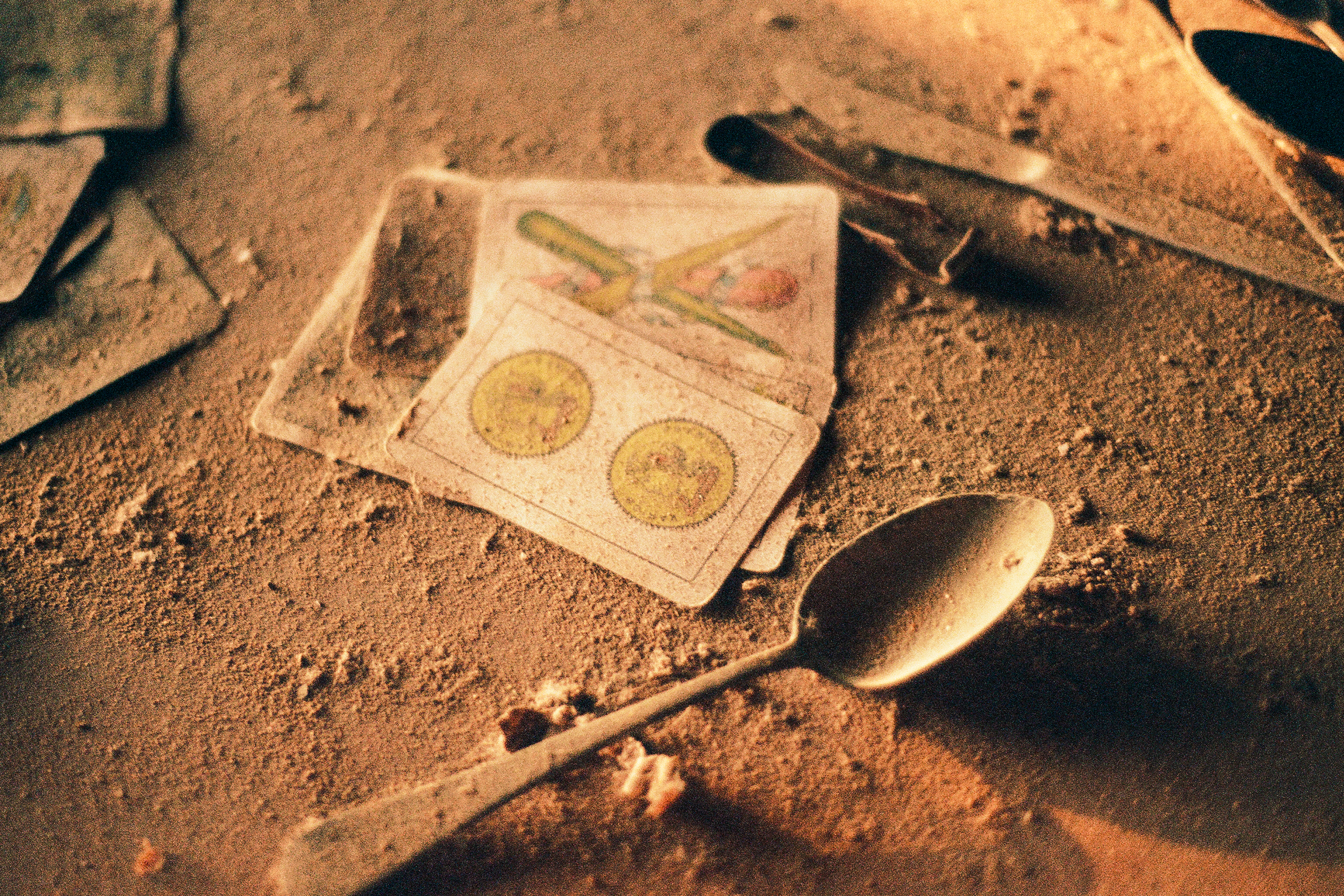 Playing cards on the dirt ground lying next to a spoon