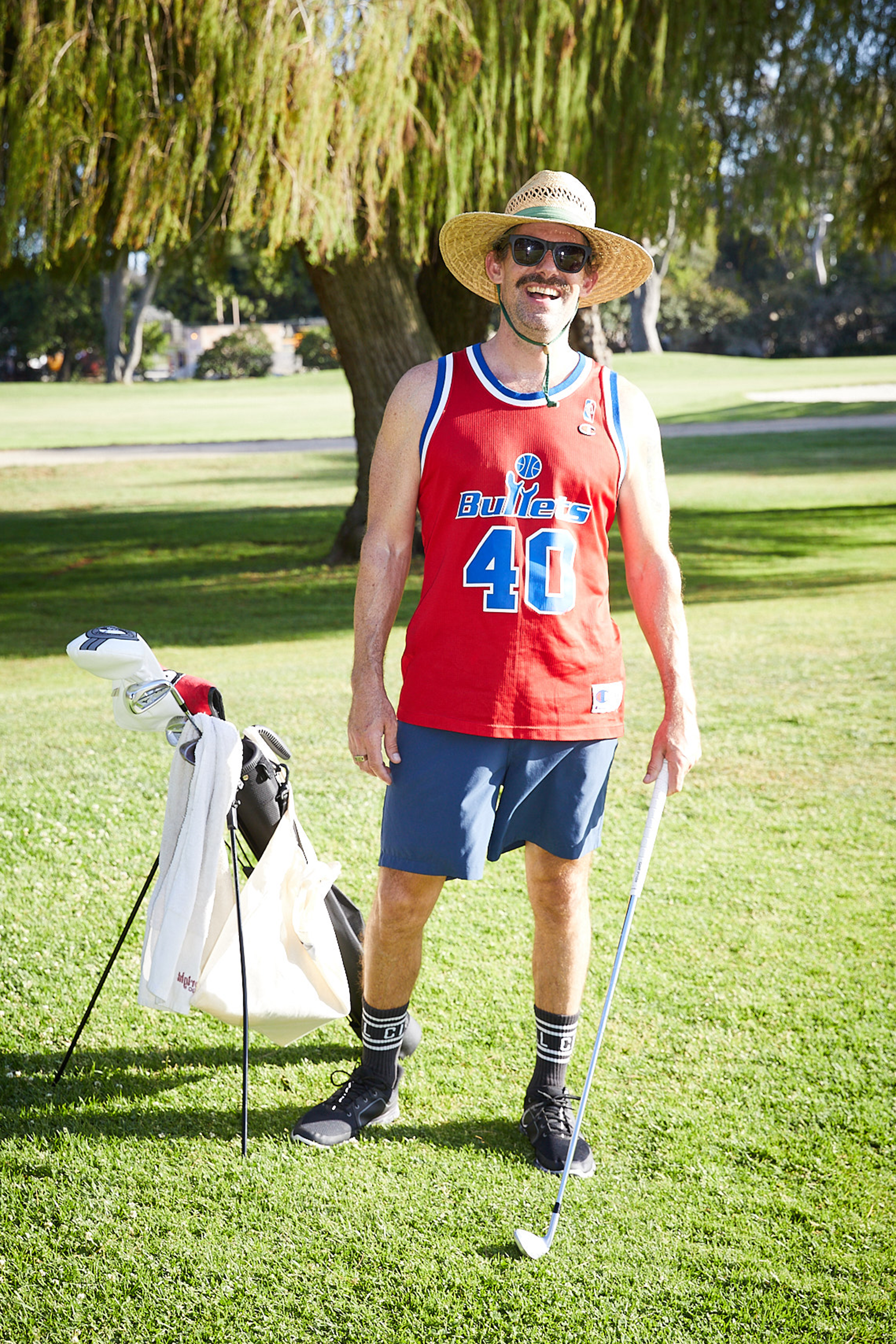 A man wearing a red jersey and a wide brim hat on the golf course