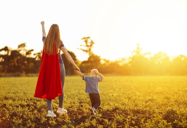 Mum with child dressed as superwoman in a field at sunset