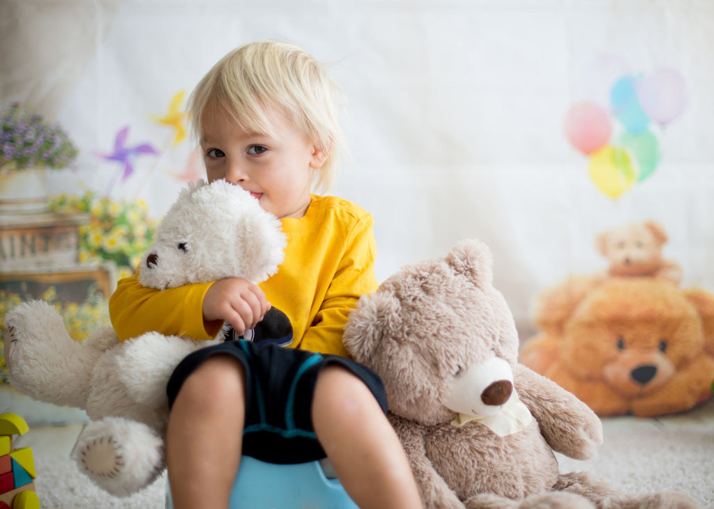 Little toddler boy sitting on a blue potty cuddling his two teddies