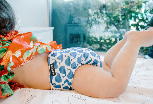 Baby on bed in snazzipants all in one cloth nappy in whale print