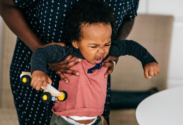 toddler crying holding toy car while parent is picking them up