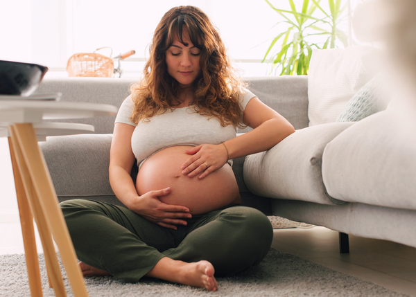 Pregnant Woman sitting on the floor in her lounge holding her pregnant belly