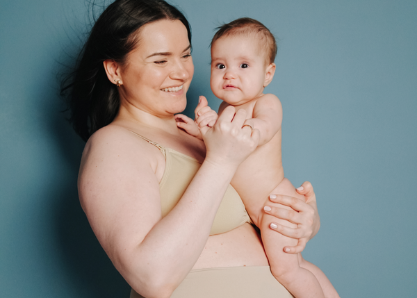 A new mother post partum, holding her newborn baby and smiling together.