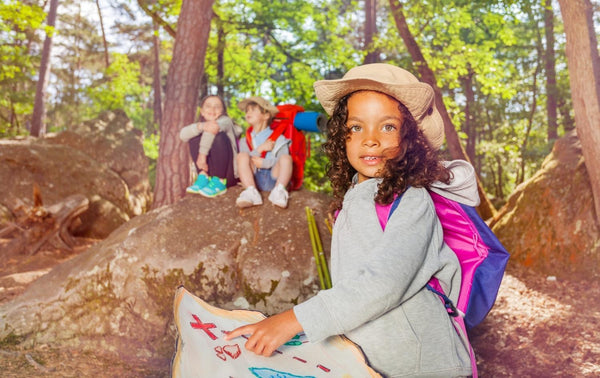 Girl at camp pointing at a map outside in a forest